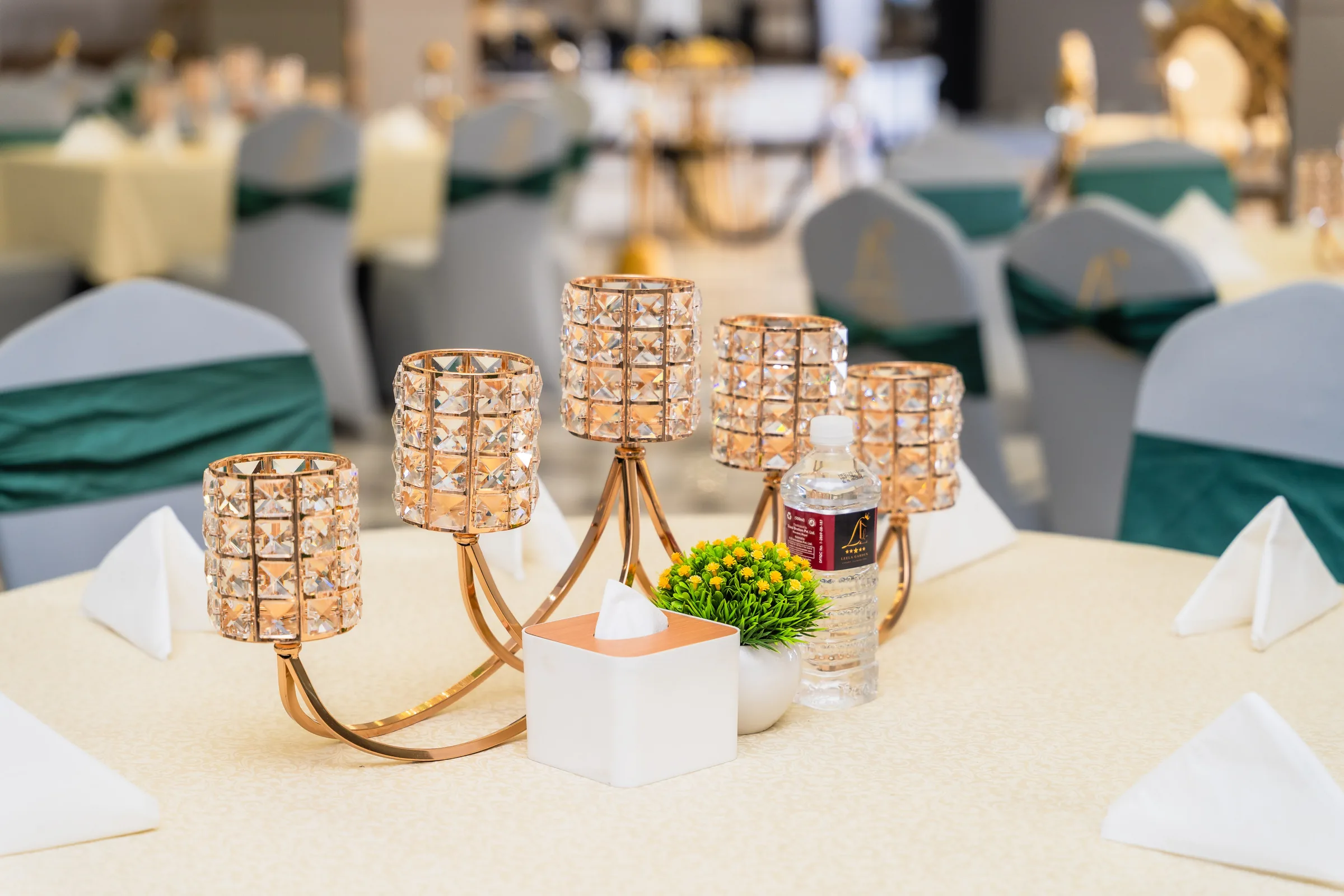 A close view of a table setting: a gold crystal candelabra centrepiece, folded napkins and deep green chair sashes.
