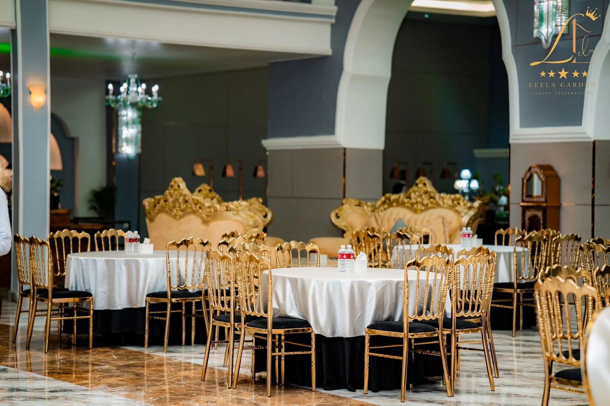 The banquet hall set for a reception, with gold chiavari chairs at linen-dressed round tables between the hall’s tall columns.